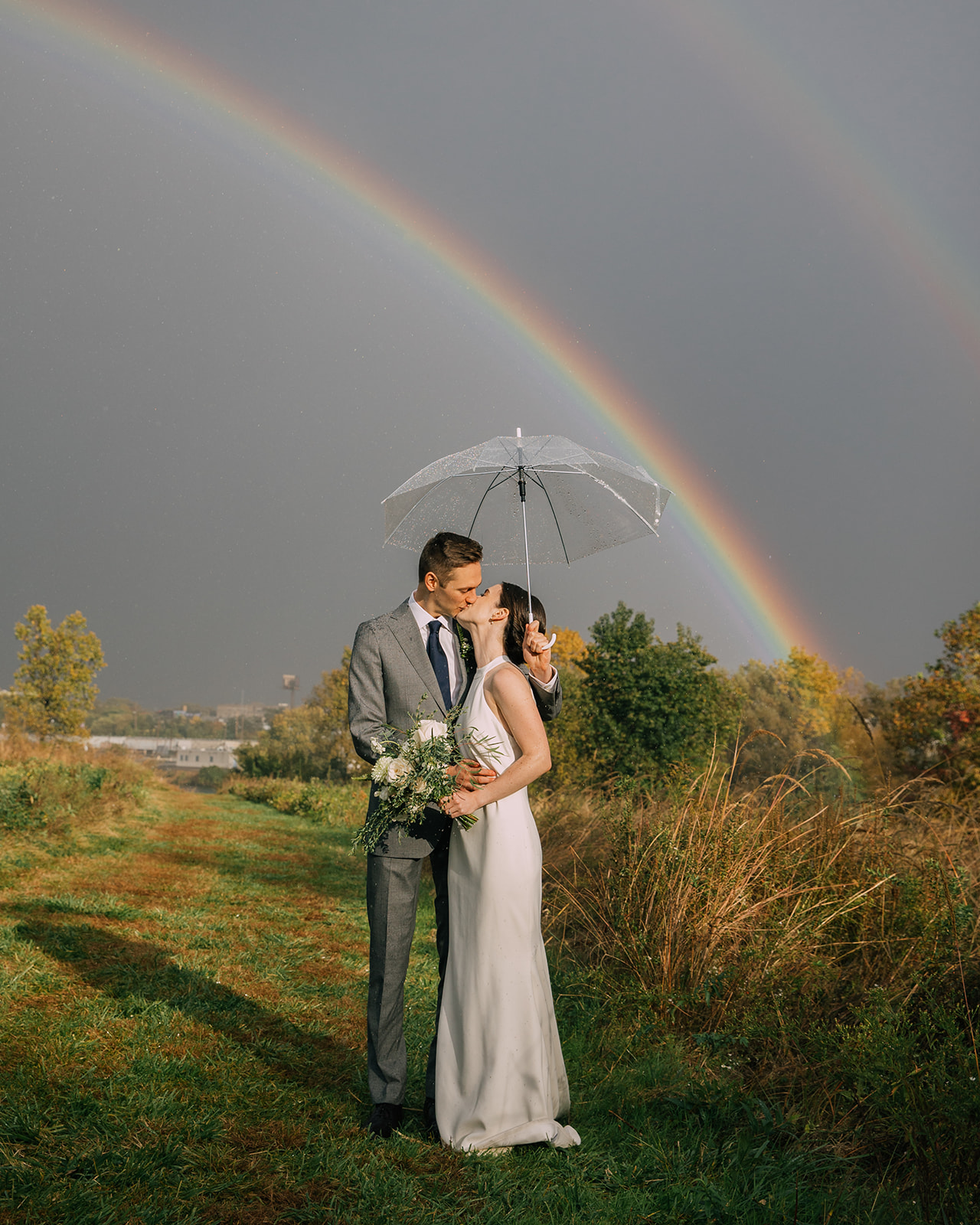 Bride and Groom kiss in rain under a rainbow